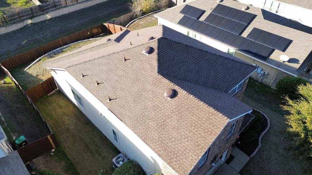 Aerial view of a house with a dark shingle roof and solar panels on adjacent homes.