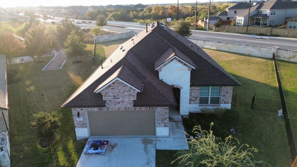 Aerial view of a modern brick home with a spacious lawn and nearby road.