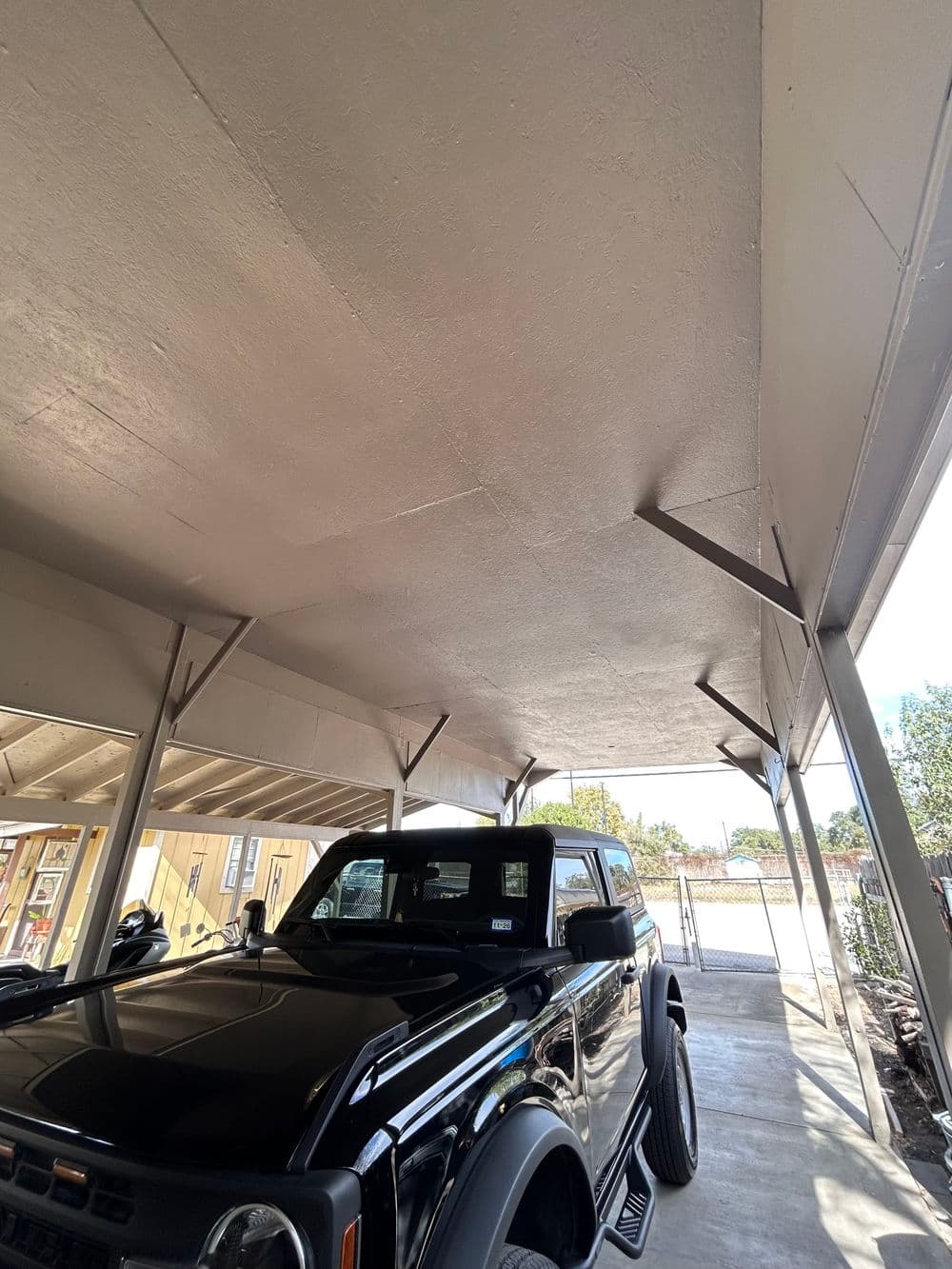 Black truck parked under a covered carport with bright sunlight streaming in.