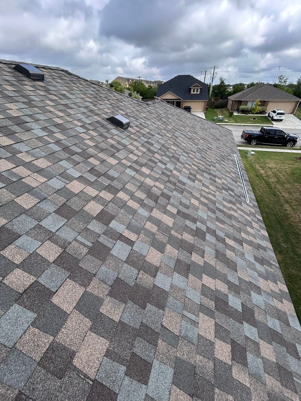 View of a sloped asphalt shingle roof under a cloudy sky, showcasing texture and color variation.